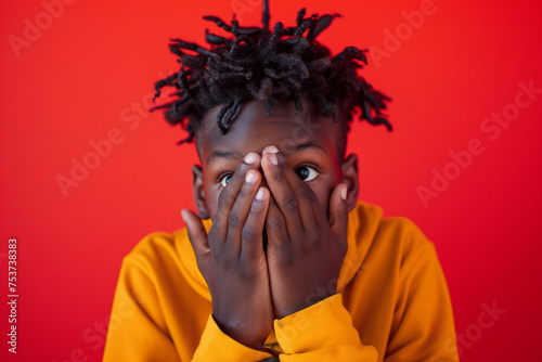 a photograph of a 18 year old african american boy who is sadly surprised holding his hands in front of his mouth, red background. AI Generated photo