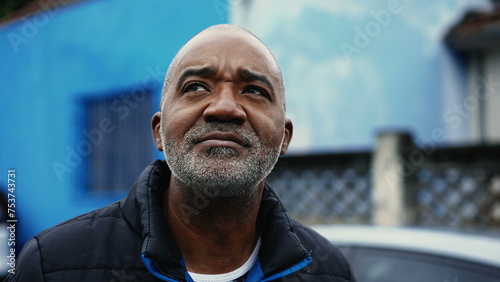 Pensive African American mature man in 50s observing urban surroundings while strolling in street, close-up face tracking shot of a black middle aged person with thoughtful gaze