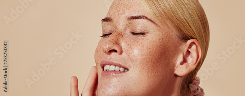 Side view of smiling blond woman with freckles touching her face. Close-up studio shot of young positive female with closed eyes against pastel background.