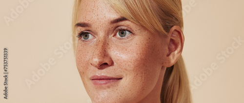 Cropped portrait of young blond woman with freckles. Female with smooth healthy skin against a pastel backdrop.