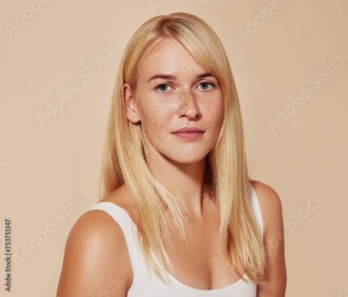 Studio portrait of a young beautiful woman with blond hair over a pastel backdrop. Female with freckled perfect skin looking at camera against a beige backdrop.