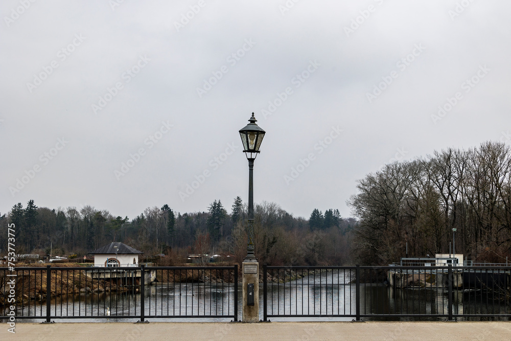 A street lamp in the centre of the bridge over the Wertach river on an iron railing on a cloudy day in the Göggingen district of Augsburg