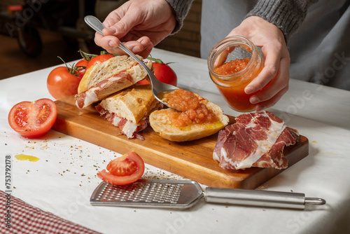 Deliciosos bocadillos de jamón serrano con tomate natural sobre tabla de madera con mujer sirviendo tomate triturado.