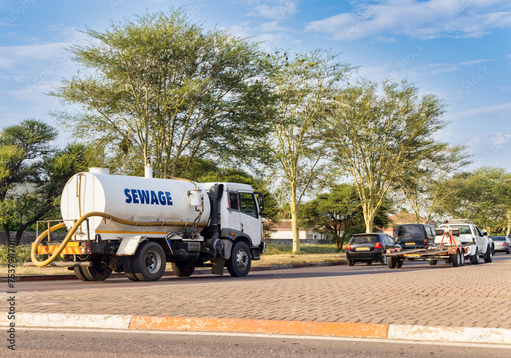 sewage truck on the road at an intersection driving behind few cars and a trailer sewage truck on the road at an intersection driving behind few cars and a trailer