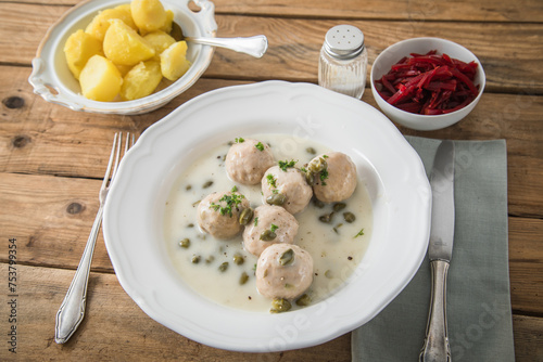 Königsberger Klopse mit Kapern, Salzkartoffeln und Rote Beete Salat auf tiefer Teller und rustikalen Holztisch mit Besteck, Salz und Serviette