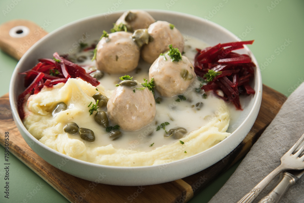 Königsberger Klopse mit Kapern, Kartoffelpüree und Rote Beete Salat in Schale mit Holzbrett, Silber Besteck und Serviette auf Hintergrund grün Königsberger Klopse mit Kapern, Kartoffelpüree und Rote Beete Salat in Schale mit Holzbrett, Silber Besteck und Serviette auf Hintergrund grün