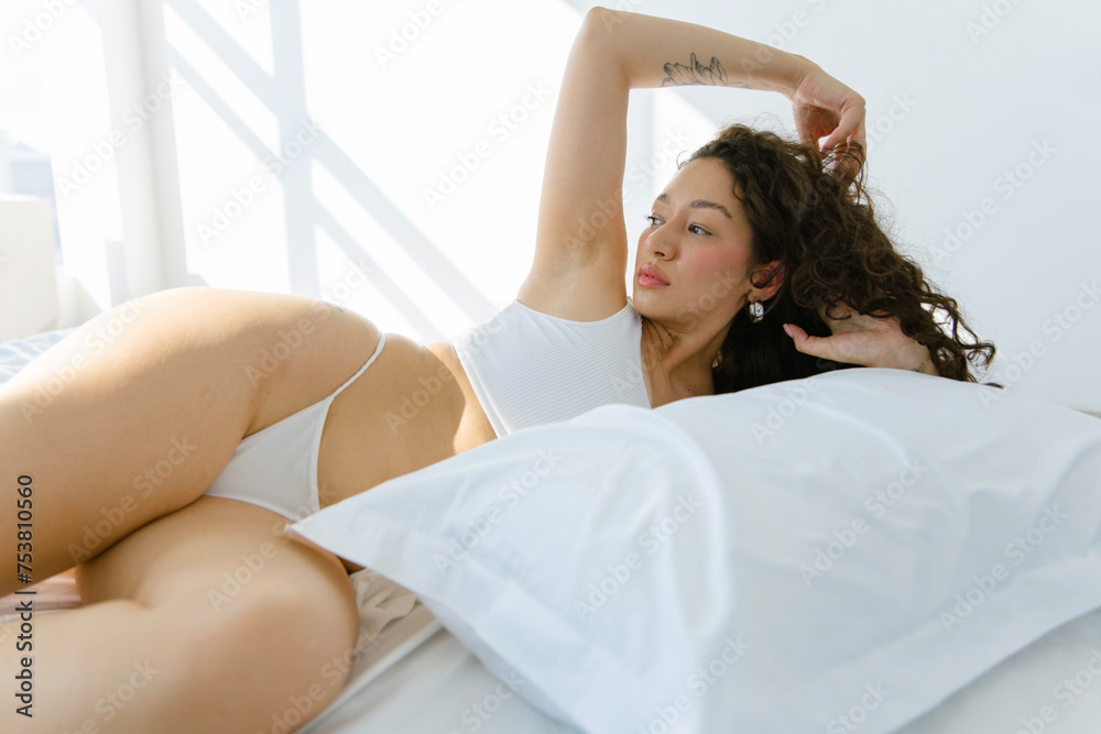 © Nikita Sursin/Stocksy - Curve woman in white underwear posing on bed © Nikita Sursin/Stocksy - Curve woman in white underwear posing on bed