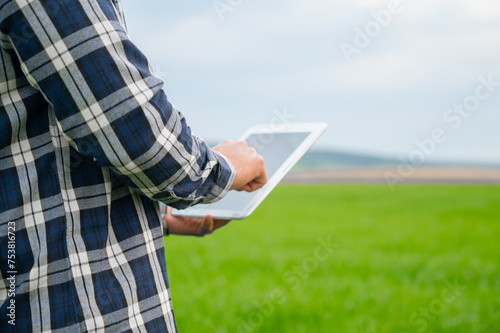Close up of a Farmer man read or analysis a report in tablet computer on a green agriculture field. High quality photo