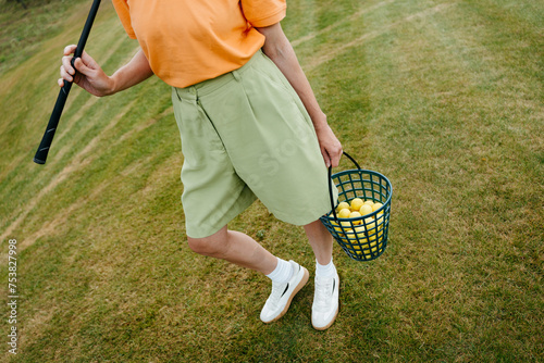 A woman with golf equipment in her hands stands on the course photo