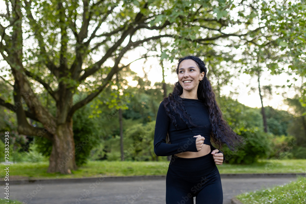 Smiling female runner in sportswear jogging in a green park at dusk, portraying the joy of outdoor exercise and well-being. Smiling female runner in sportswear jogging in a green park at dusk, portraying the joy of outdoor exercise and well-being.