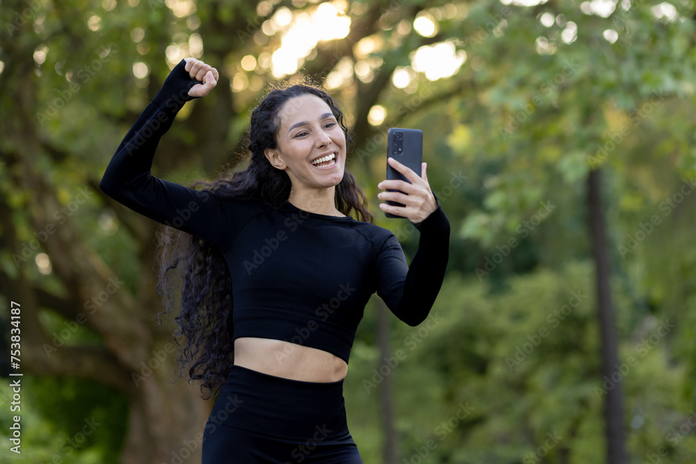 Smiling, active female in athletic attire captures a cheerful moment on her phone, embodying health and happiness. Smiling, active female in athletic attire captures a cheerful moment on her phone, embodying health and happiness.