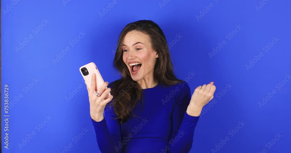 Attractive brunette woman look surprised wow hold mobile cell phone on blue background. Girl look on smartphone and doing winner gesture. Girl just found out big win news, wow, mobile phone victory. Attractive brunette woman look surprised wow hold mobile cell phone on blue background. Girl look on smartphone and doing winner gesture. Girl just found out big win news, wow, mobile phone victory.