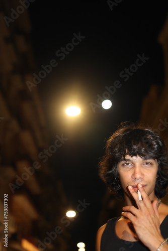 Rocker smoking a cigarette on the street at night with street lamps photo