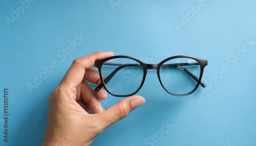 Hand with eyeglasses composition on blue background.