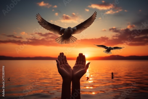 Hands open palm up worship with birds flying over calm water sunset background. Concept of praying for blessing from God. © Kristina