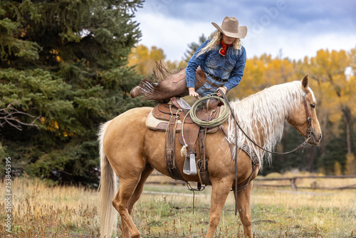 Colorado Cowgirl mounting a palomino horse in the mountains with colorful aspens in the background