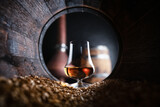 A glass of bourbon whiskey in old oak barrel. Copper alambic and oak barrel on background. Traditional alcohol distillery concept