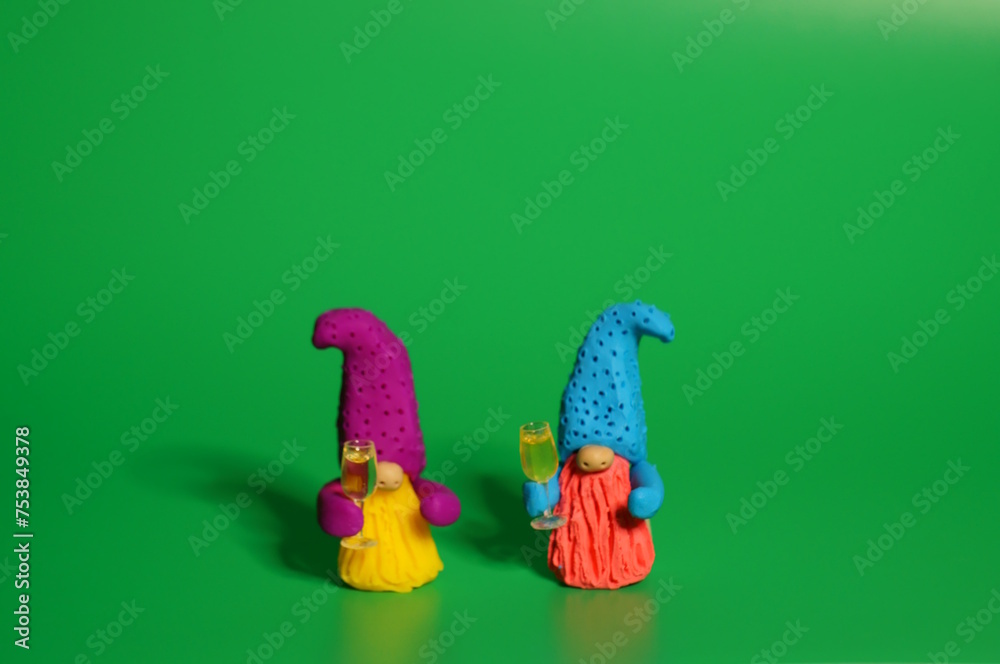 Two toy dwarfs made of plasticine with glasses of champagne. New Year's holidays and Christmas. Decorations and decorations. Green background.