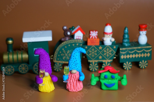 Two toy dwarfs made of plasticine with glasses of champagne on the background of a Christmas train. New Year's holidays and Christmas. Decorations and decorations.