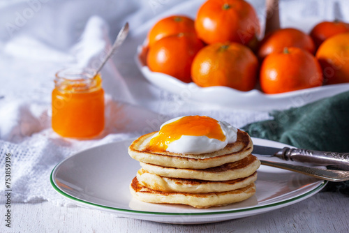 Obraz na płótnie Pancakes served with tangerine jam and sour cream, and tangerines on a light background. w salonie