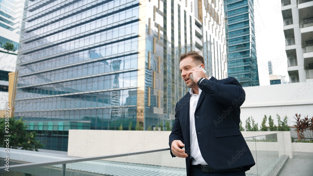 Skilled businessman talking to marketing team about marketing strategy by using phone while standing at skyscraper. Happy manager calling colleague about increasing sales at modern urban city. Urbane.