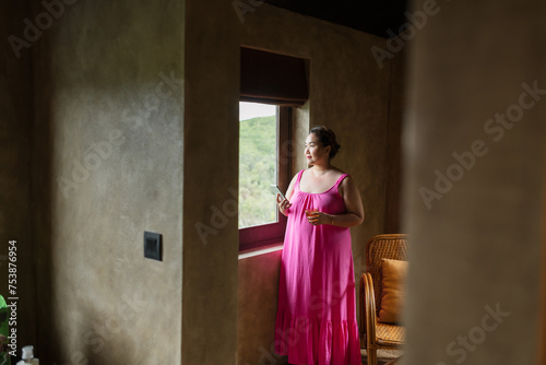 Woman talking on cellphone standing near window looking aside photo