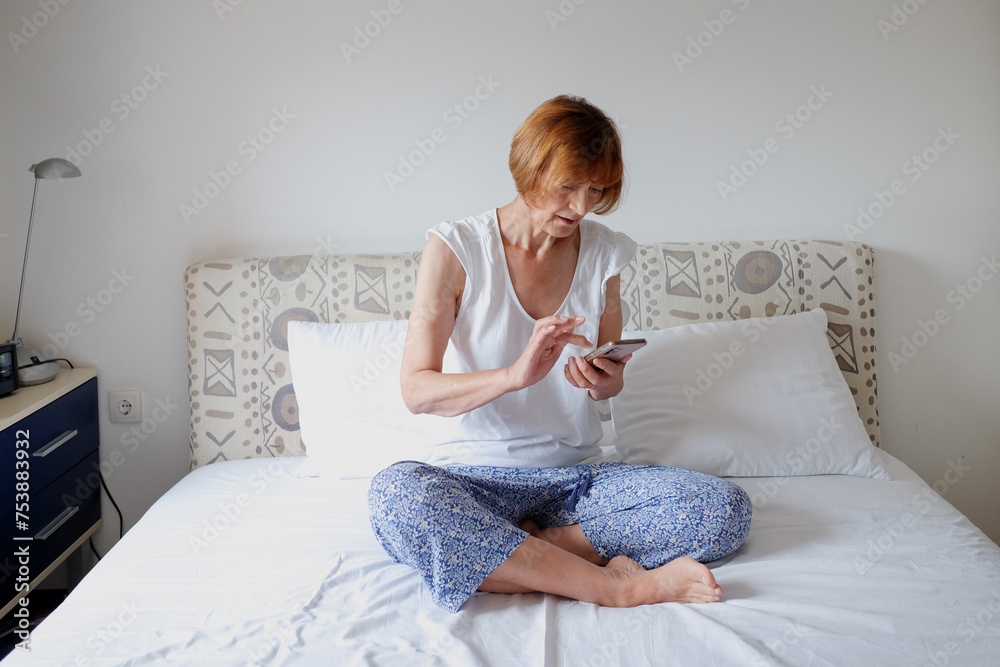 Mature woman texting on a mobile phone during morning in bedroom Mature woman texting on a mobile phone during morning in bedroom