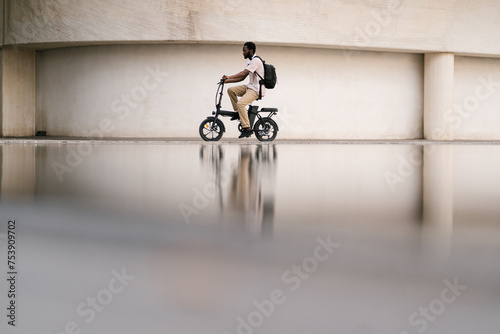 Male college student riding electric bike by building photo