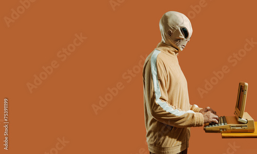 man wearing an alien mask uses an old computer