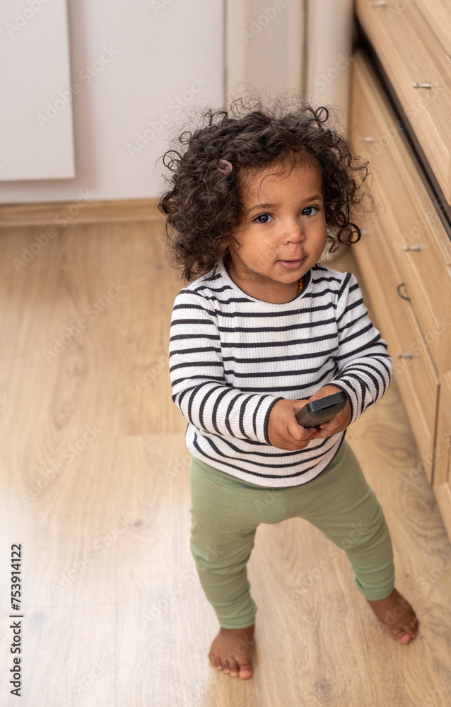 A mixed race curious toddler holds a TV remote, symbolizing the early interaction with digital devices in modern childhood, and development. A mixed race curious toddler holds a TV remote, symbolizing the early interaction with digital devices in modern childhood, and development.