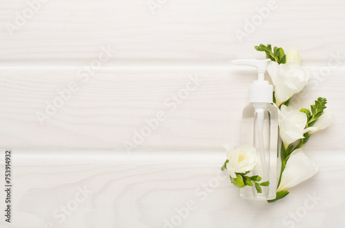 Cosmetic bottle with freesia flowers on wooden background, top view