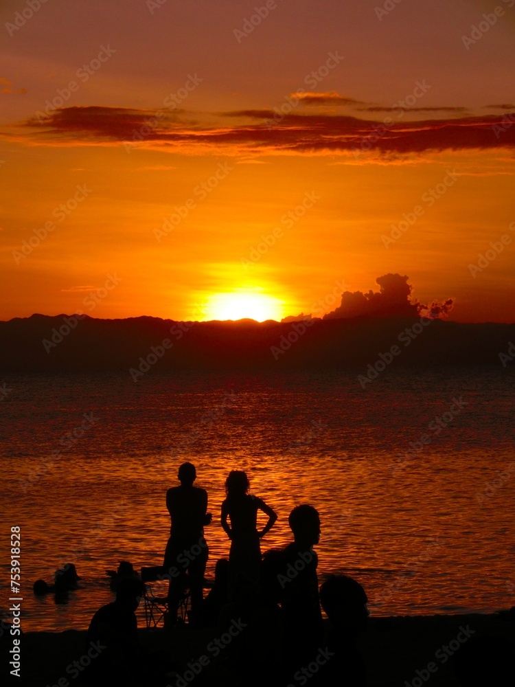 Vertical shot of a silhouette of a group of people relaxing on a sandy beach by the sea