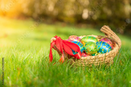 Easter eggs in basket in grass. Colorful decorated easter eggs in wicker basket. Traditional egg hunt for spring holidays. Morning magical light. 