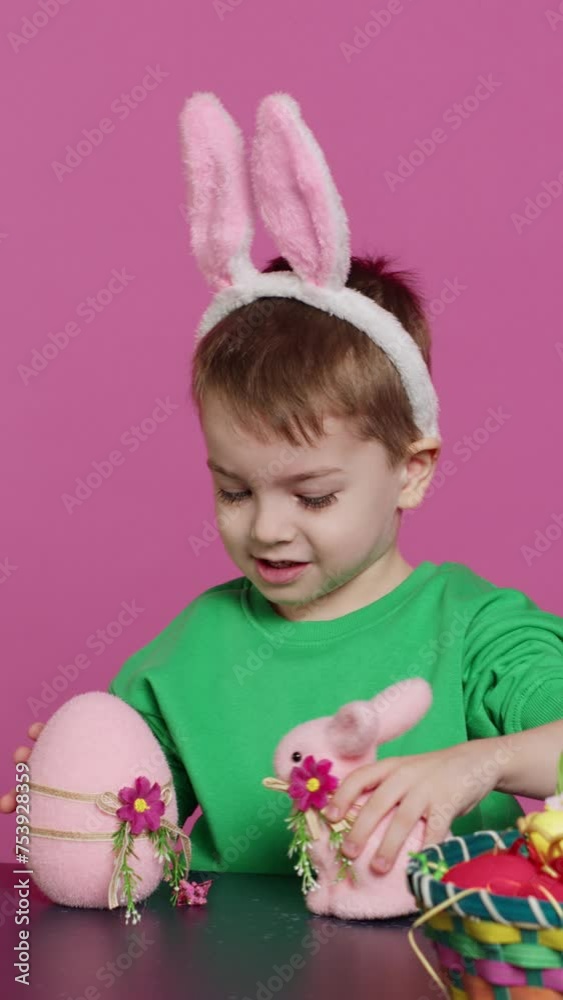 Vertical Video Joyful young kid playing around with festive painted decorations, showing a rabbit toy and a pink egg in front of camera. Smiling small boy with bunny ears having fun with ornaments Vertical Video Joyful young kid playing around with festive painted decorations, showing a rabbit toy and a pink egg in front of camera. Smiling small boy with bunny ears having fun with ornaments