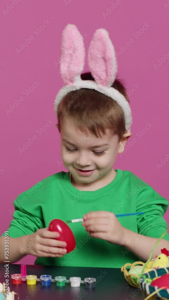 Vertical Video Smiling jolly preschooler painting eggs and ornaments for easter festivity preparations, using art and craft materials to decorate festive arrangements. Young boy having fun with tie Vertical Video Smiling jolly preschooler painting eggs and ornaments for easter festivity preparations, using art and craft materials to decorate festive arrangements. Young boy having fun with tie