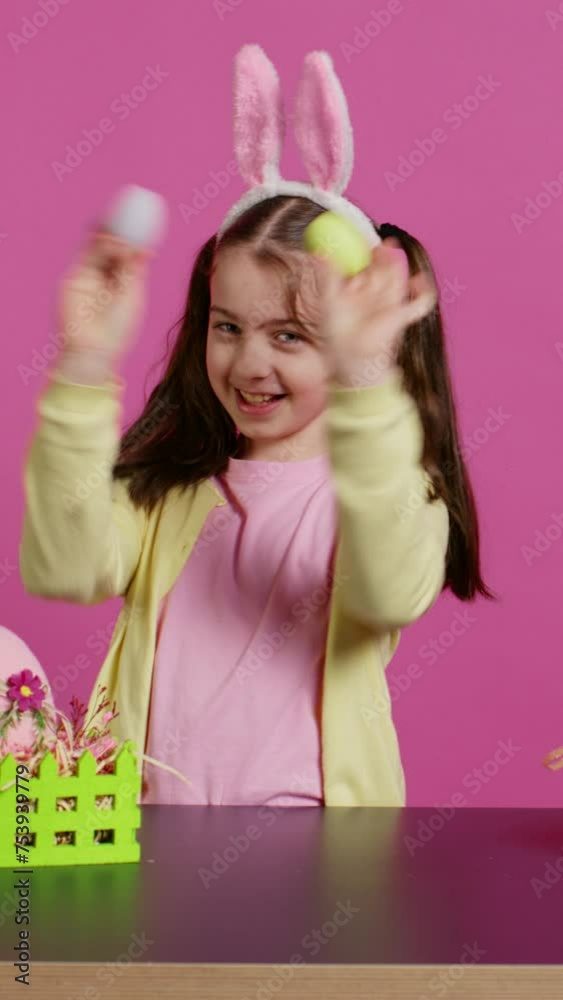 Enthusiastic young girl playing peek a boo in front of camera, using painted easter eggs against pink background. Joyful lovely toddler feeling excited about spring holiday festivity. Camera B. Enthusiastic young girl playing peek a boo in front of camera, using painted easter eggs against pink background. Joyful lovely toddler feeling excited about spring holiday festivity. Camera B.