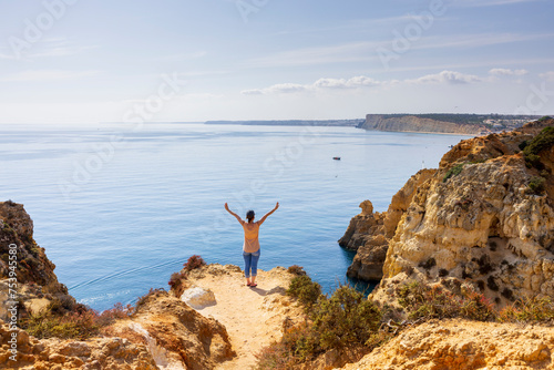 Young woman standing on the edge of cliff with wide arms open and looking at the sea. Ponta da Piedade, Lagos, Algarve, Portugal