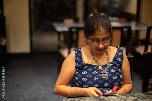Middle aged Indian woman browsing smartphone inside a house photo