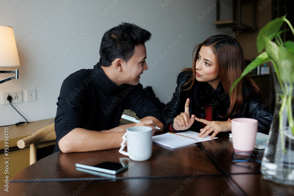 Young couple discussing and taking notes on a diary indoors Young couple discussing and taking notes on a diary indoors