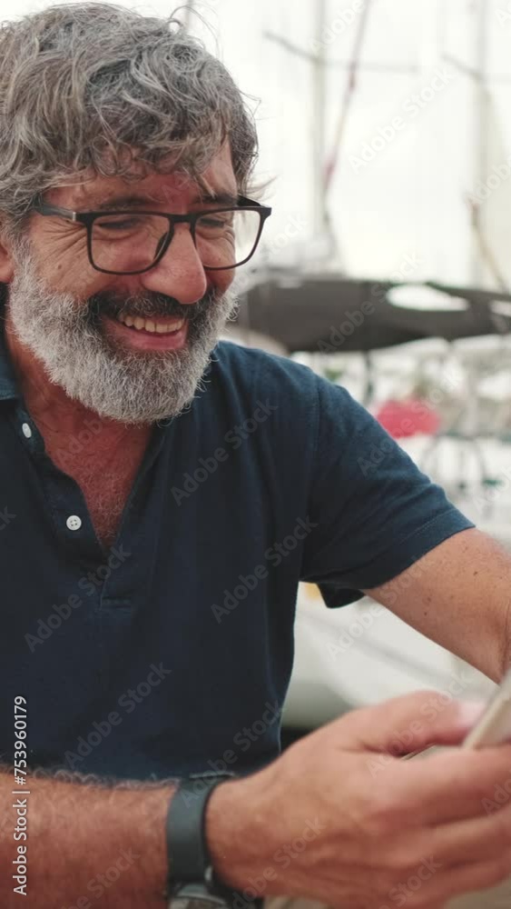 Smiling aged man sitting in port uses phone