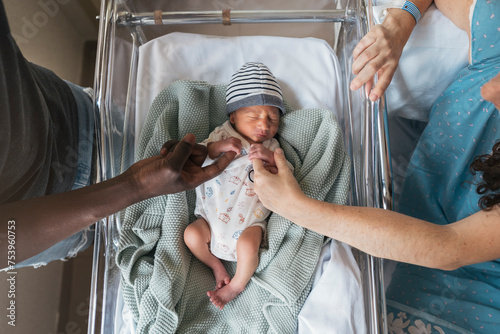Parents holding hands their newborn baby on the crib