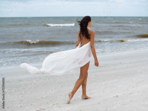 Thoughtful romantic beach woman in white dress walking in stormy windy weather