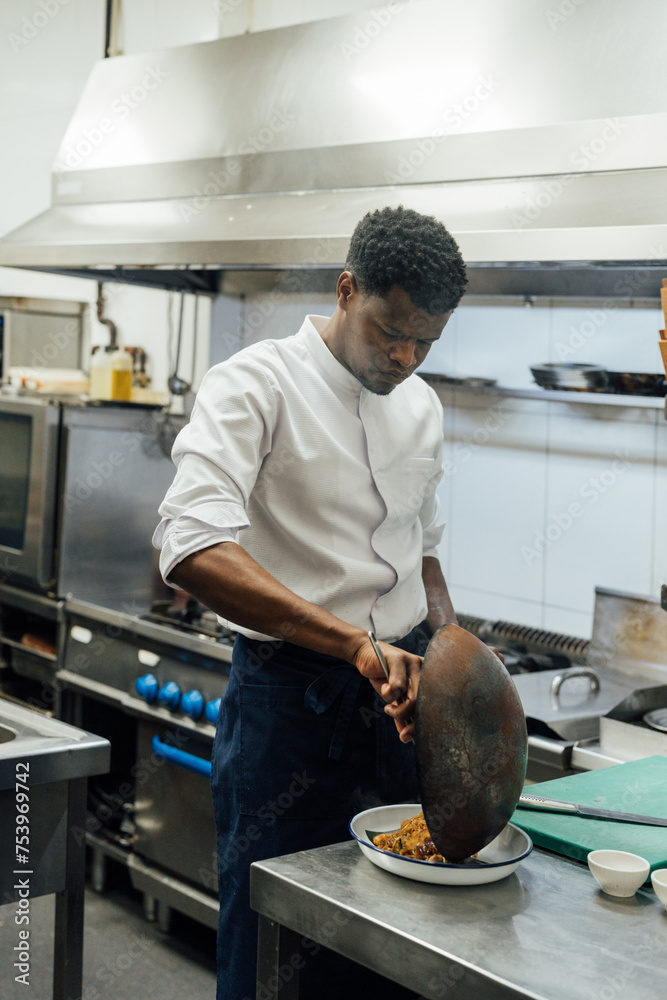 Focused African American cook putting food from wok Focused African American cook putting food from wok