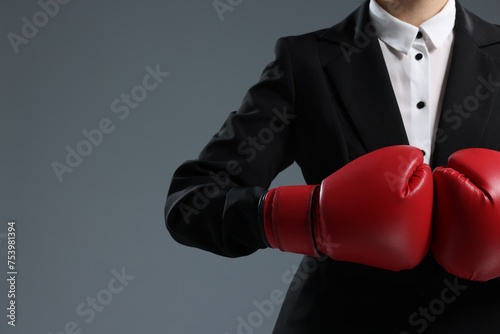 Businesswoman in suit wearing boxing gloves on grey background, closeup. Space for text © New Africa