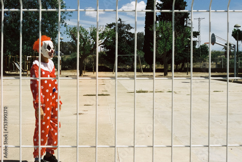 scary clown standing in an outdoors sports court, 35mm photo