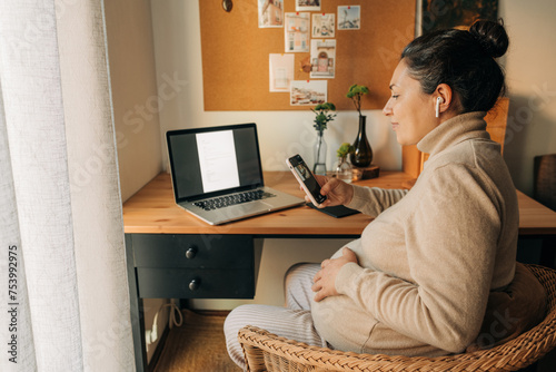 Pregnant woman looking at her phone sitting at the desk photo