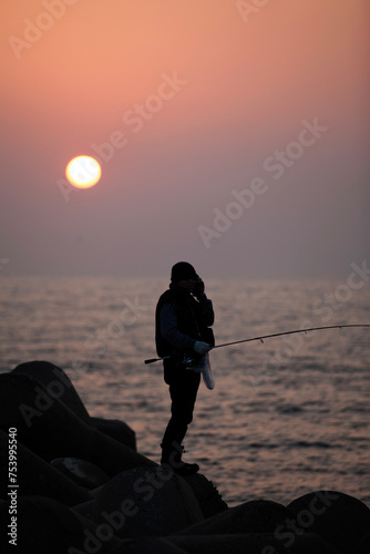 Sunset view with the silhouettes of fishing people on the seawall