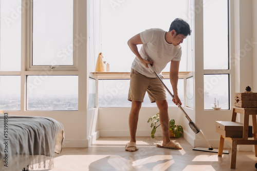 Asian Thai man using mop for cleaning floor in living room apartment, Man do household chores, housework concept. marriage life.