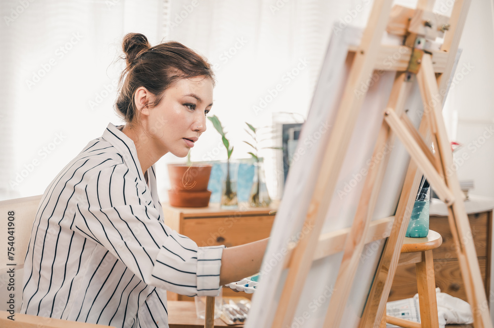 Portrait photo of young beautiful Asian woman artist painting water color art picture in indoor studio.