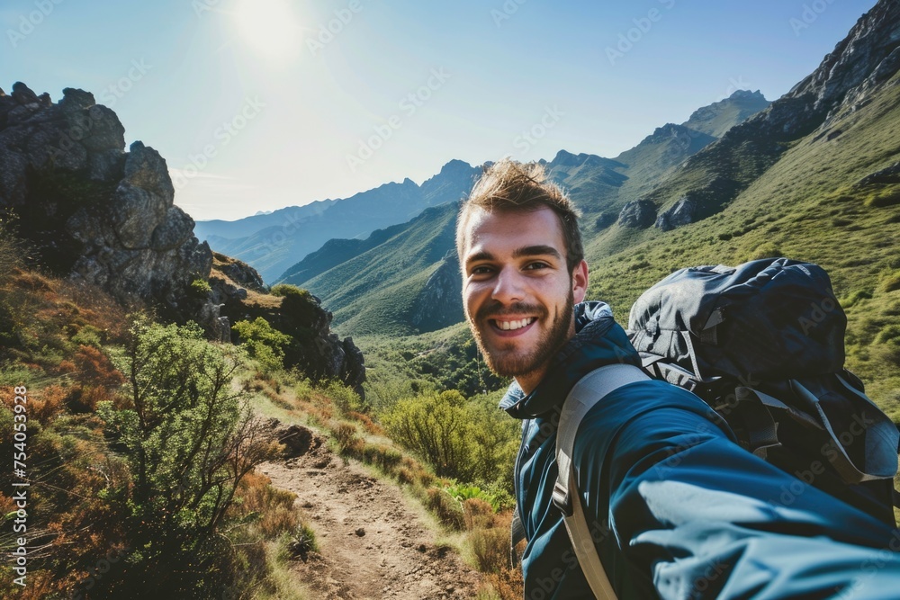 A cheerful young man takes a selfie picture atop a mountain, capturing the joy of his outdoor adventure.